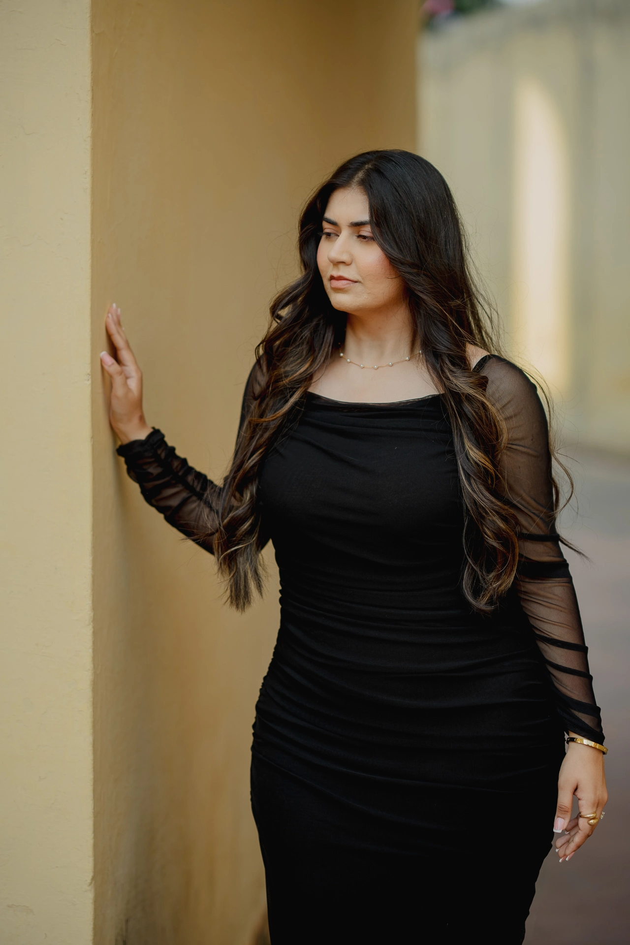 Woman standing alone against a stone wall, black dress