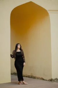 Woman standing alone in a mustard archway, black outfit