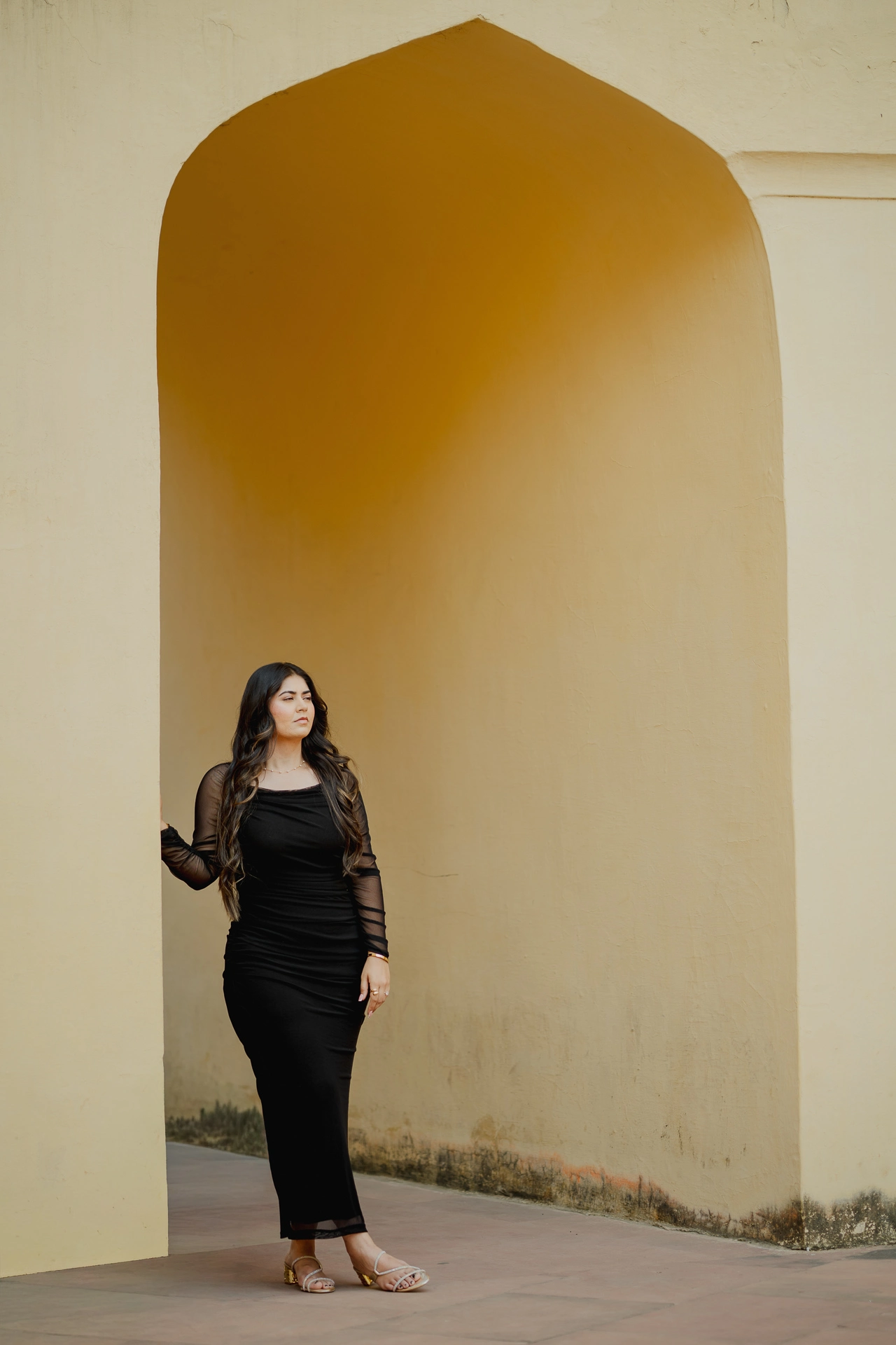 Woman standing alone in a mustard archway, black outfit